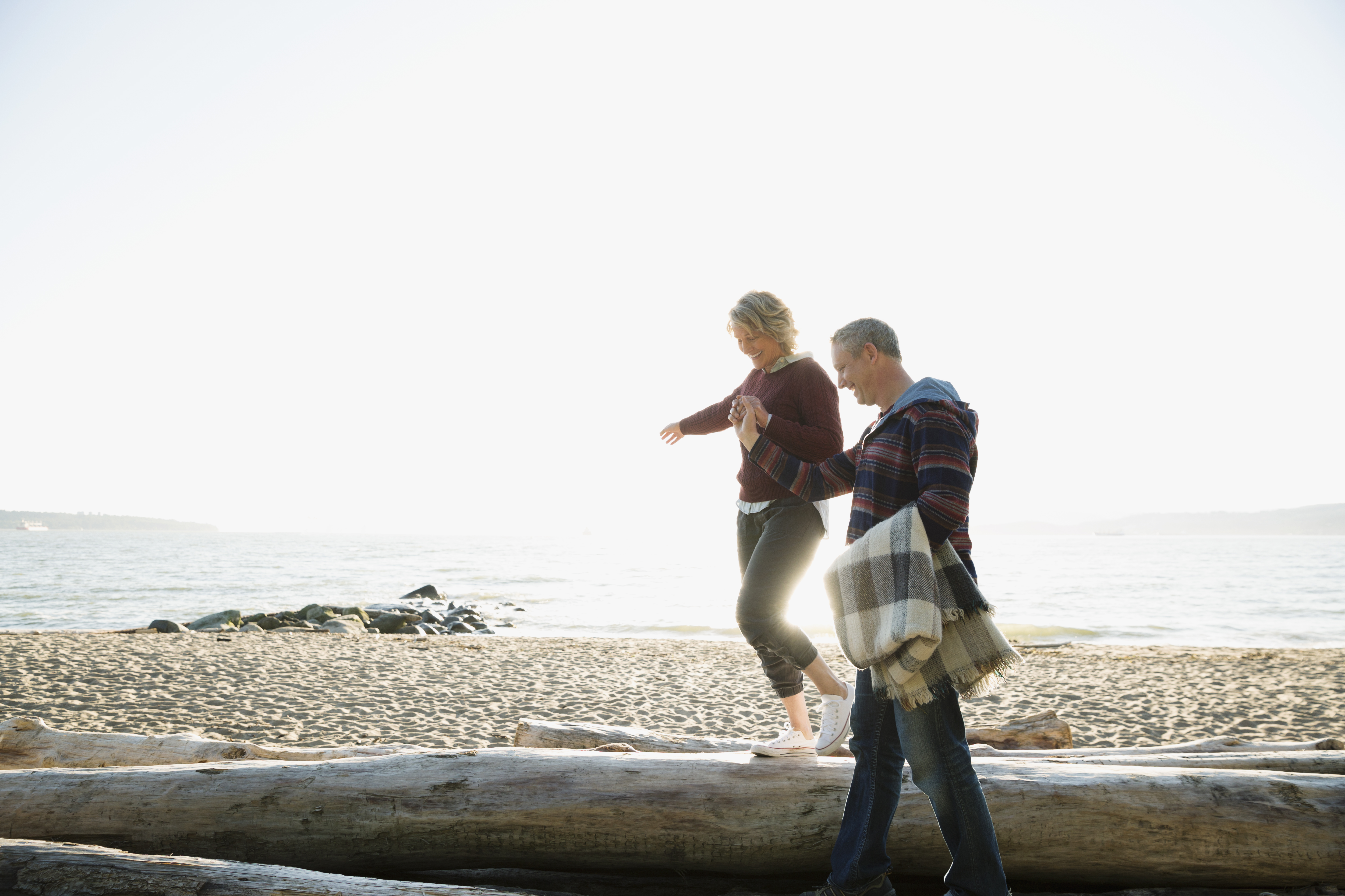 Couple holding hands walking balancing on driftwood on sunny beach